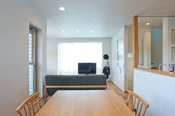 リビングの扉を開けると居室までフラットで繋がるので、坪数以上に広々と感じられます ソファーの正面の窓はテラスに繋がり、ブラインド越しに光と木々の緑を感じられます。